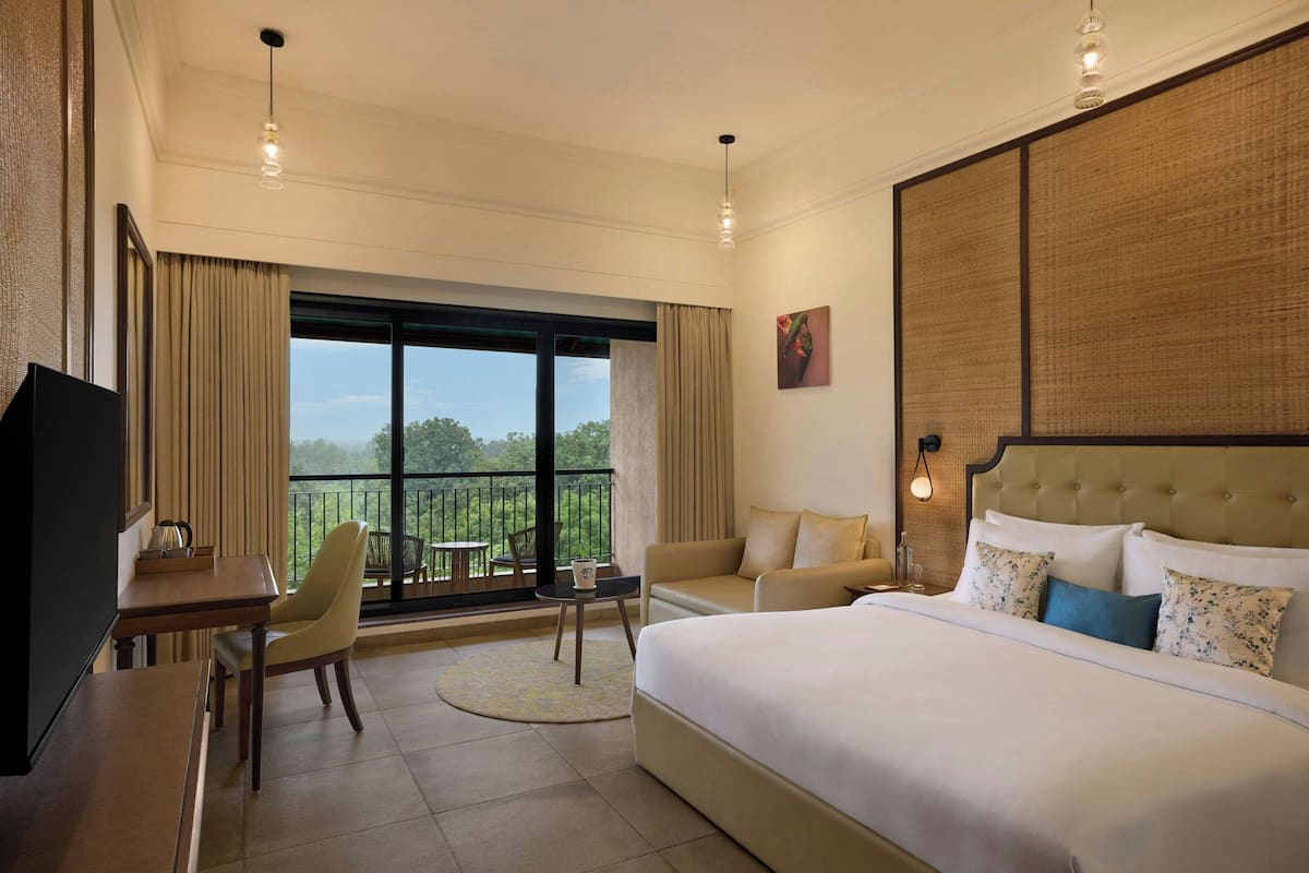 Habitación de hotel con una cama grande, un escritorio, una silla, un balcón con mesa y sillas, y vistas al exterior.