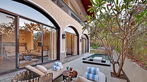 A luxurious outdoor seating area with wicker furniture, a small table with a drink, and a pool in the background.
