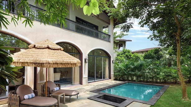 A poolside area with lounge chairs, a thatched umbrella, and a swimming pool.