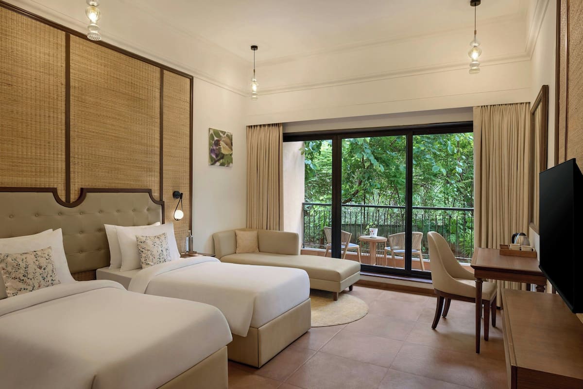 Habitación de hotel con dos camas, un sofá, un televisor y un balcón con vistas a zonas verdes.