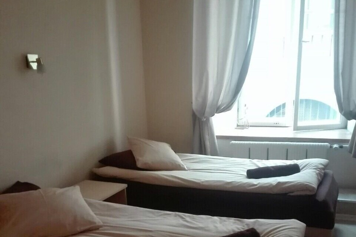 A hotel room with two single beds, a window with curtains, and a radiator.