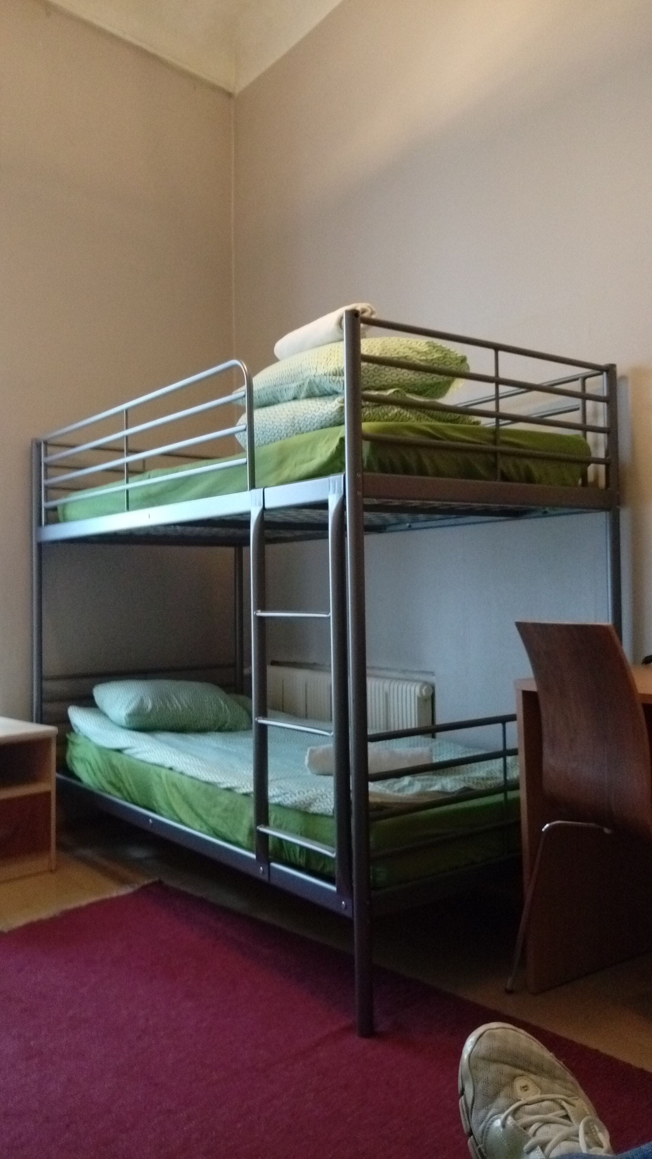 A bunk bed with a desk and chair, a radiator, and a red carpet.