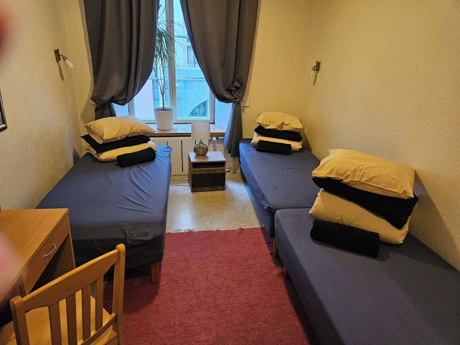 A small, compact room with two single beds, a small table, and a chair.