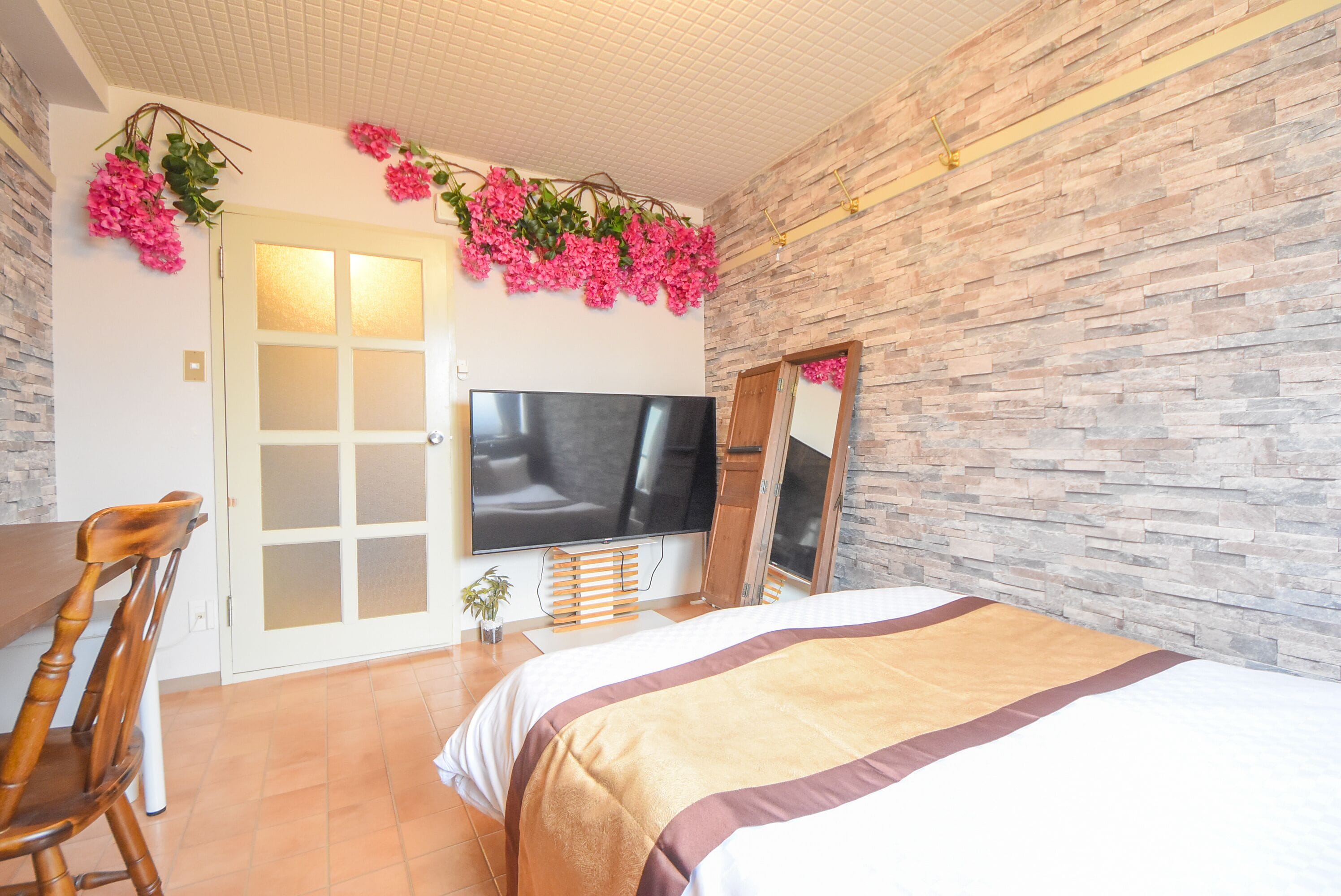 A bedroom with a bed, a TV, a wooden chair, and a stone wall.