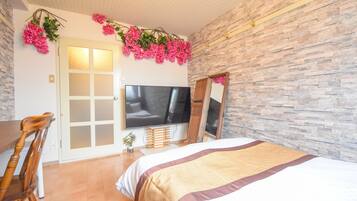 A bedroom with a bed, a TV, a wooden chair, and a stone wall.