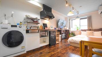 Habitación pequeña y luminosa con lavadora, kitchenette, cama y comedor.