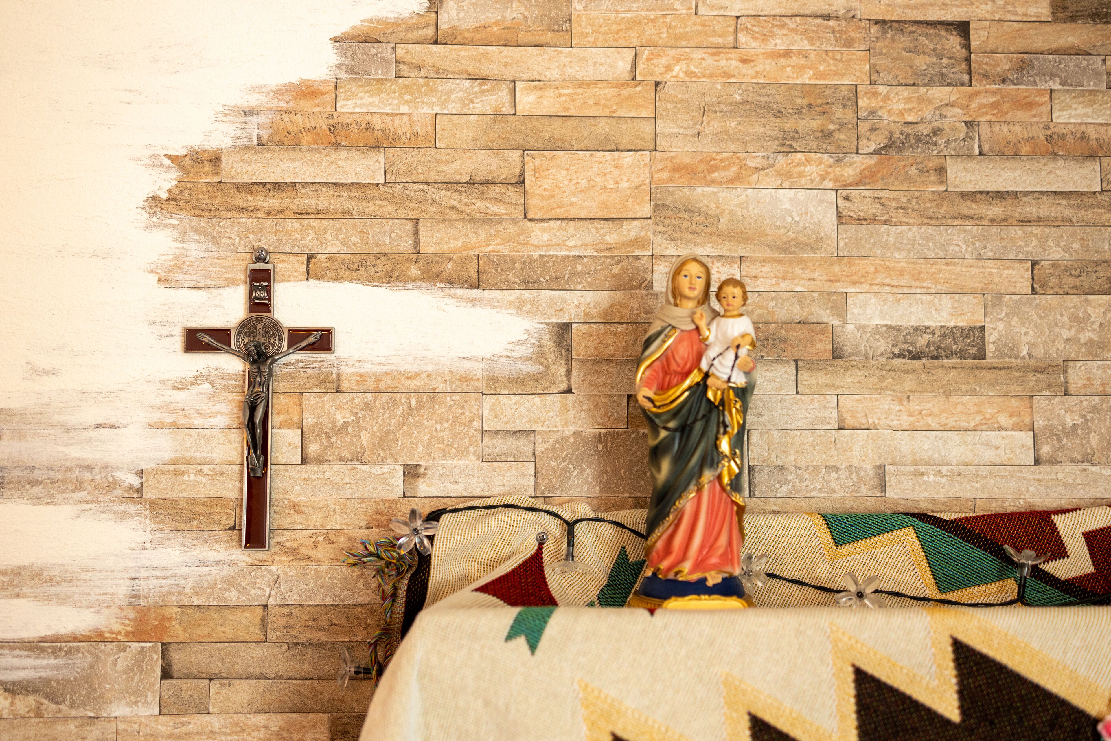 Een stenen muur met een kruis en een standbeeld van de Maagd Maria.