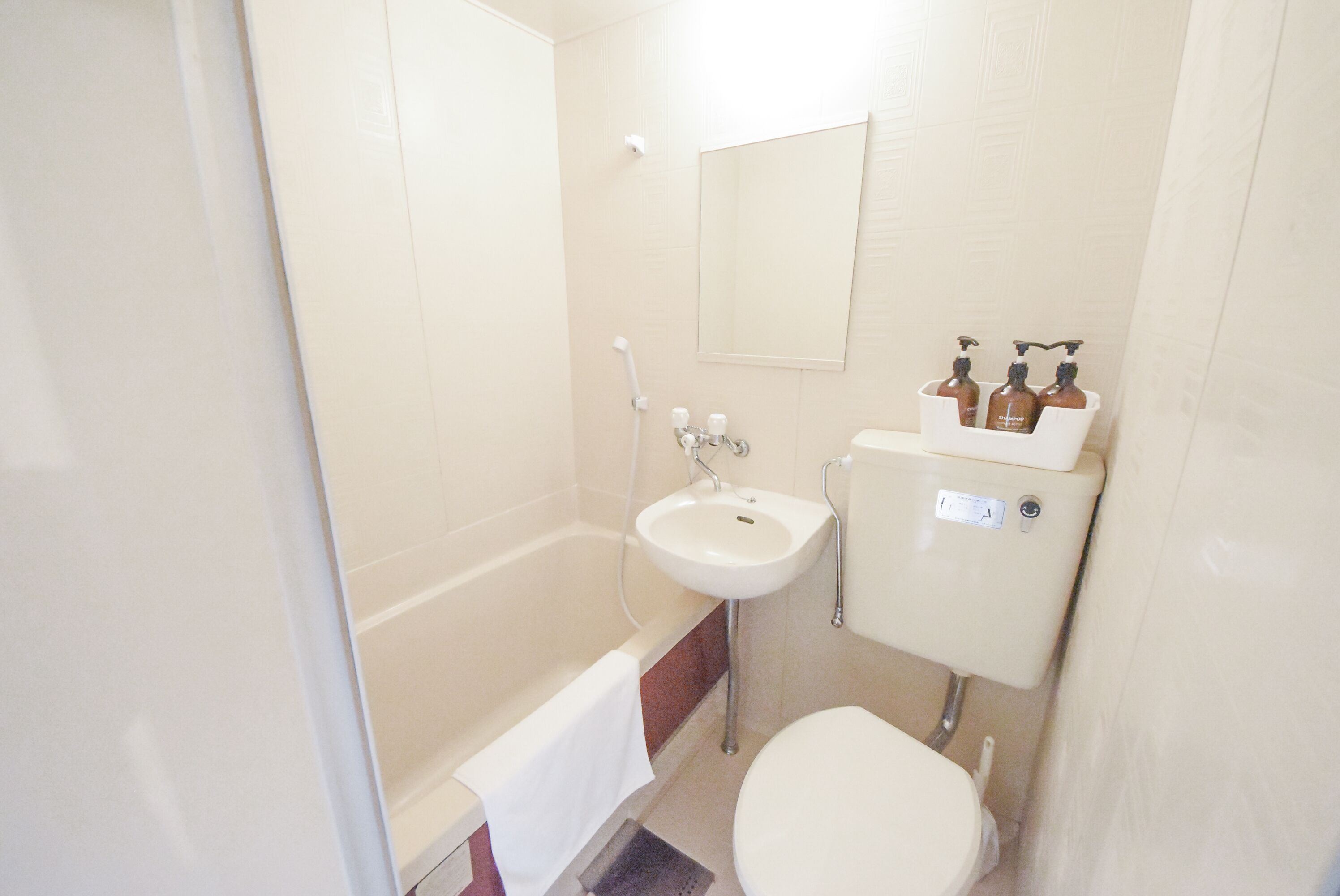 A small, compact bathroom with a white bathtub, a sink, and a toilet. There are three bottles of toiletries on the sink.