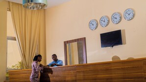 A reception area with a wooden counter, a large mirror, and three wall clocks. - Amor Hotel Ekiti (Ado Ekiti)