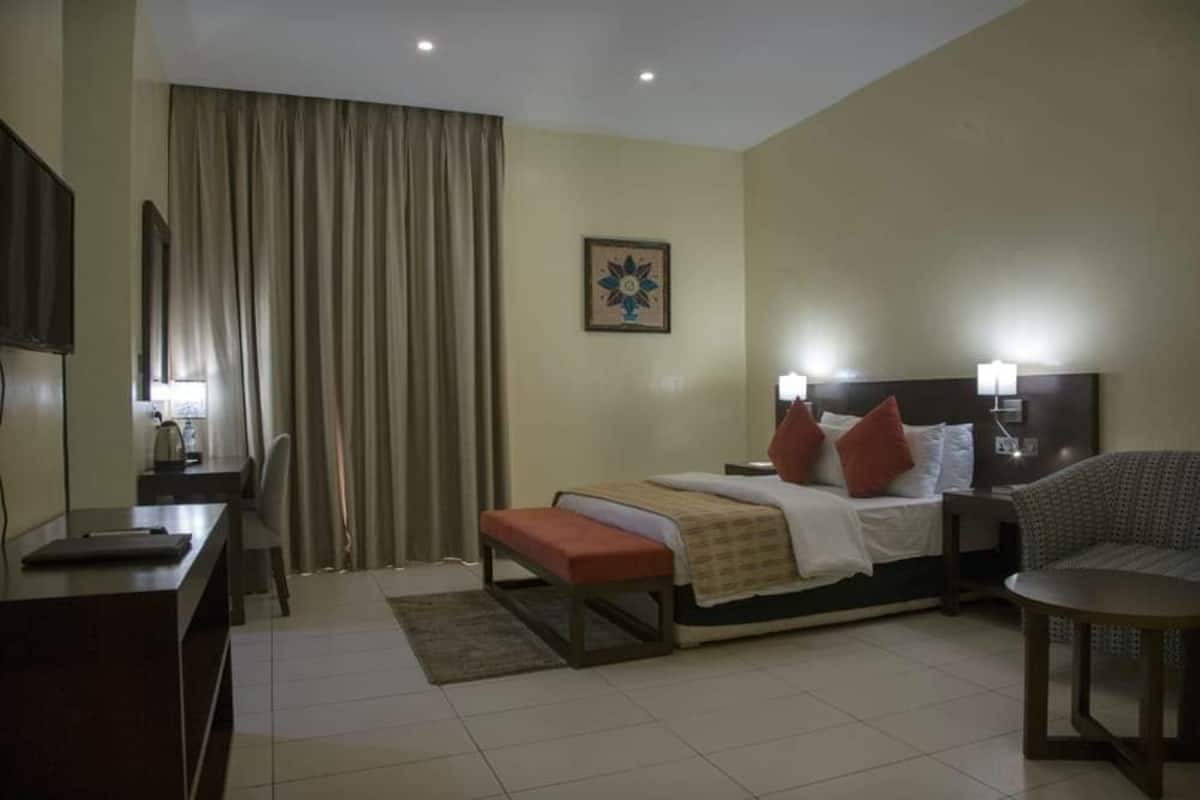 A hotel room with a bed, bedside table, desk, chair, and a small table.