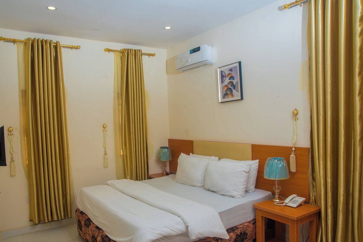 A hotel room with a bed, a nightstand with a lamp, and curtains.