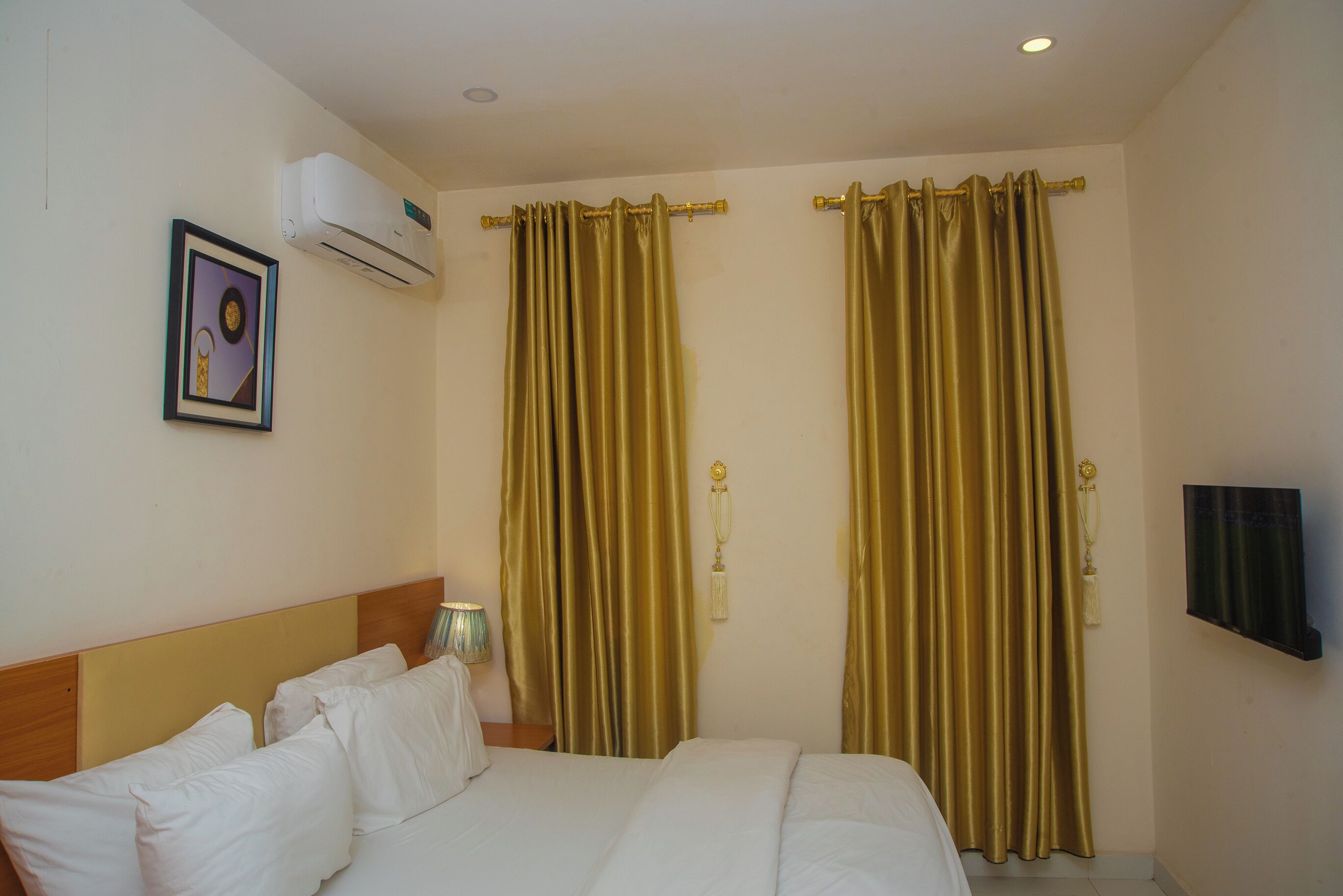 Une chambre d’hôtel avec un lit, un climatiseur fixé au mur, un tableau encadré et des rideaux.