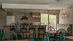A dining area with green chairs and a wooden table, a kitchen with a refrigerator and stove, and a view of the outdoors through a glass door. - Lovely 2 bedroom condo with nice amenities and on the bus line (Rochester)