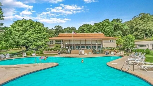 A swimming pool with lounge chairs and a building with a flag in the background. - Lovely 2 bedroom condo with nice amenities and on the bus line (Rochester)