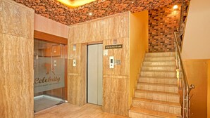 A hotel lobby with a marble wall, a glass door entrance to a restaurant, and a staircase with metal railings. - Treebo Royal Cm - City Center (Jaipur)