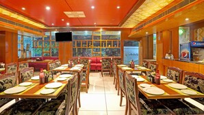 A restaurant with multiple dining tables and booths, a large window with decorative items, and a Pepsi vending machine. - Treebo Royal Cm - City Center (Jaipur)