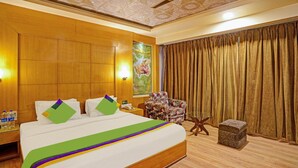 A hotel room with a large bed, a floral armchair, a small side table, and a large window with curtains. - Treebo Royal Cm - City Center (Jaipur)