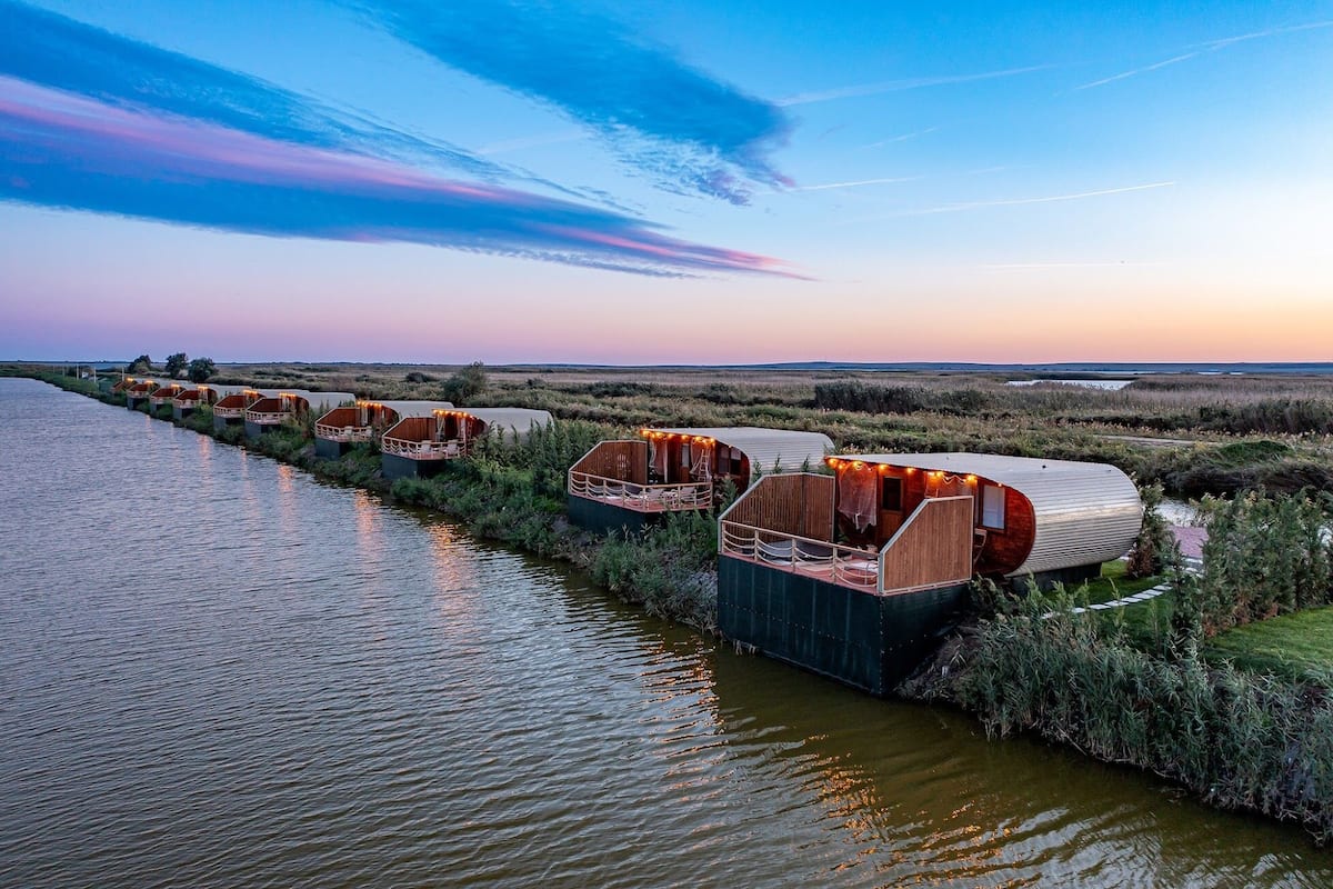 A row of floating accommodations along a river, each with a covered deck and seating area.