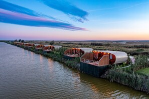 A row of floating accommodations along a river, each with a covered deck and seating area.