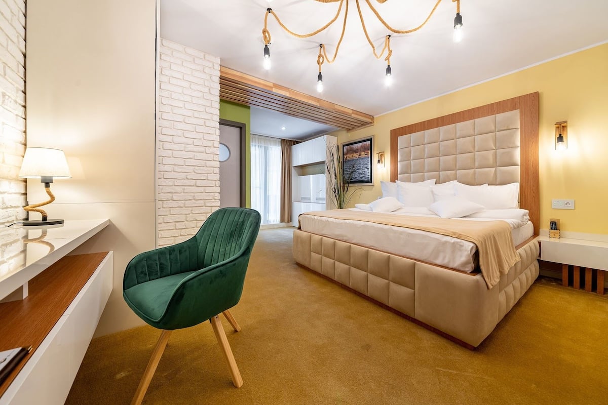 A modern hotel room with a bed, a desk, and a green chair.