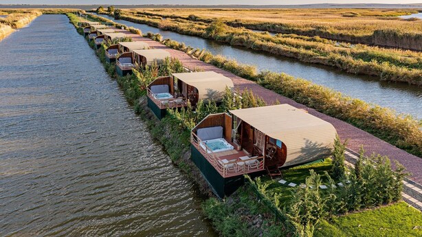 A row of floating wooden cabins with attached hot tubs, aligned along a narrow water channel. - Razelm Luxury Resort (Jurilovca)