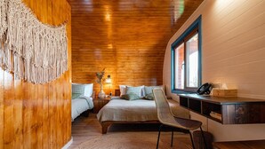 A cozy cabin-style room with wooden walls, a bed with checkered bedding, a wicker chair, and a desk with a phone and box. - Razelm Luxury Resort (Jurilovca)