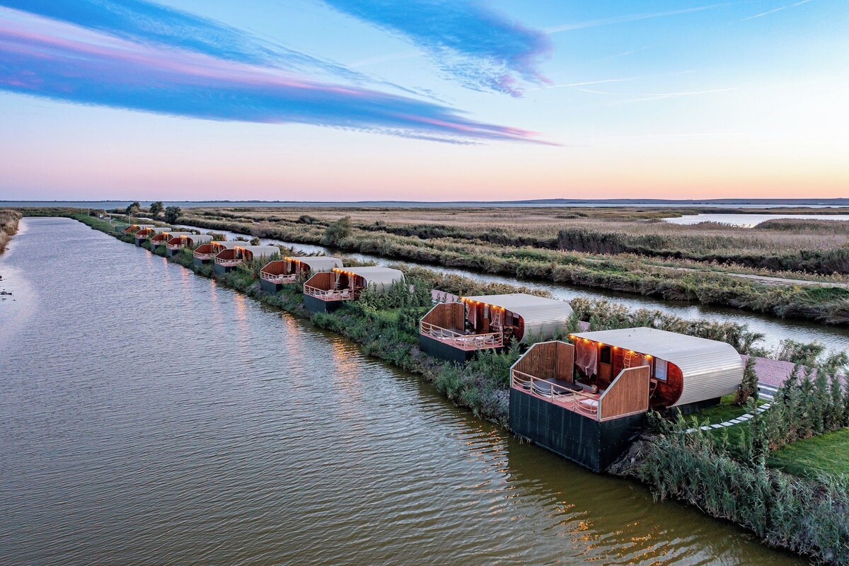 A series of hexagonal floating structures aligned along a waterway, each with a covered seating area and a small deck.