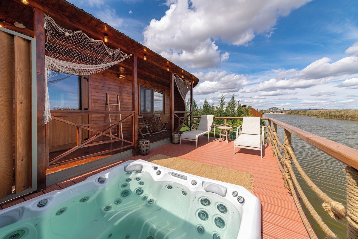 Uma cabana de madeira com hidromassagem, área de estar externa e vista para um rio.