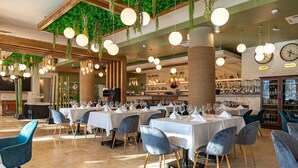 A restaurant with multiple tables set for dining, hanging plants, and a clock on the wall. - Razelm Luxury Resort (Jurilovca)