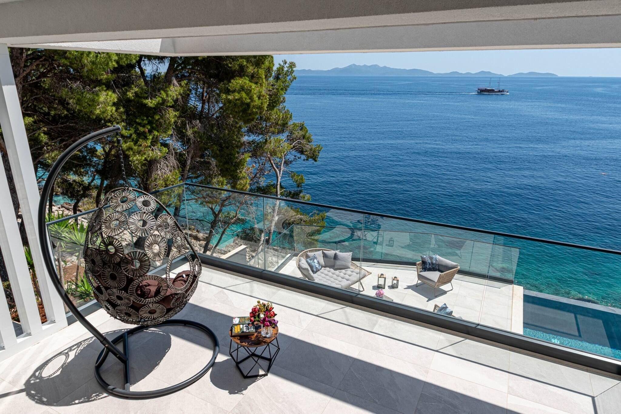 Ein Balkon mit Meerblick, ein Korbstuhl, ein kleiner Tisch mit Blumen und eine Couch.