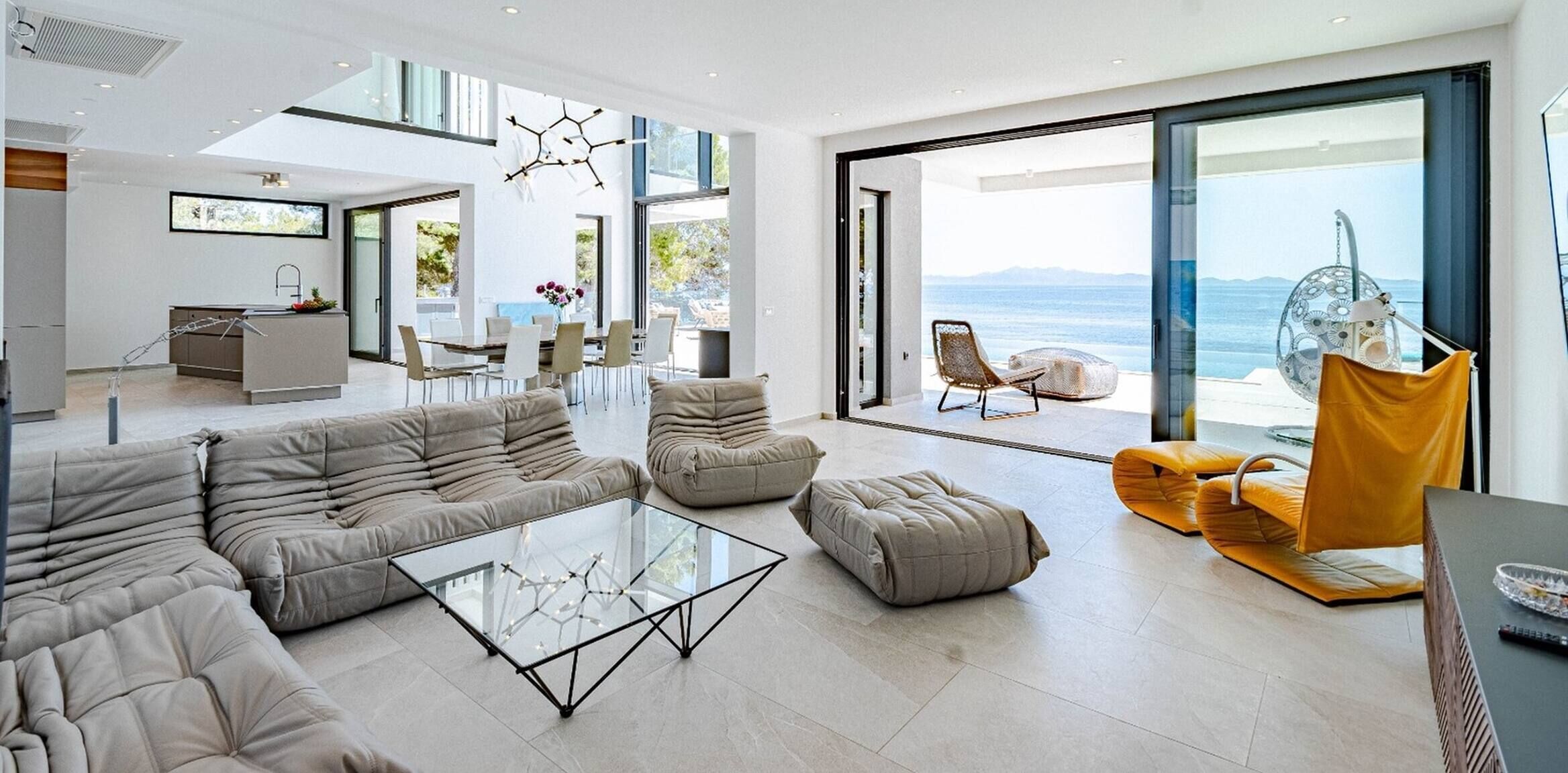 Ein modernes Wohnzimmer mit einem Glastisch, Sofas und Meerblick durch große Schiebetüren.
