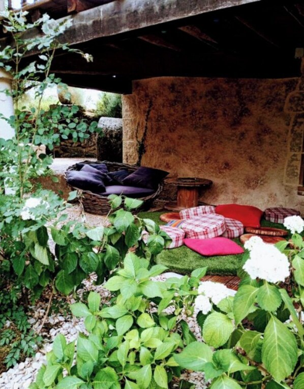 A rustic outdoor seating area with a stone wall, a woven basket, and a small wooden stool.