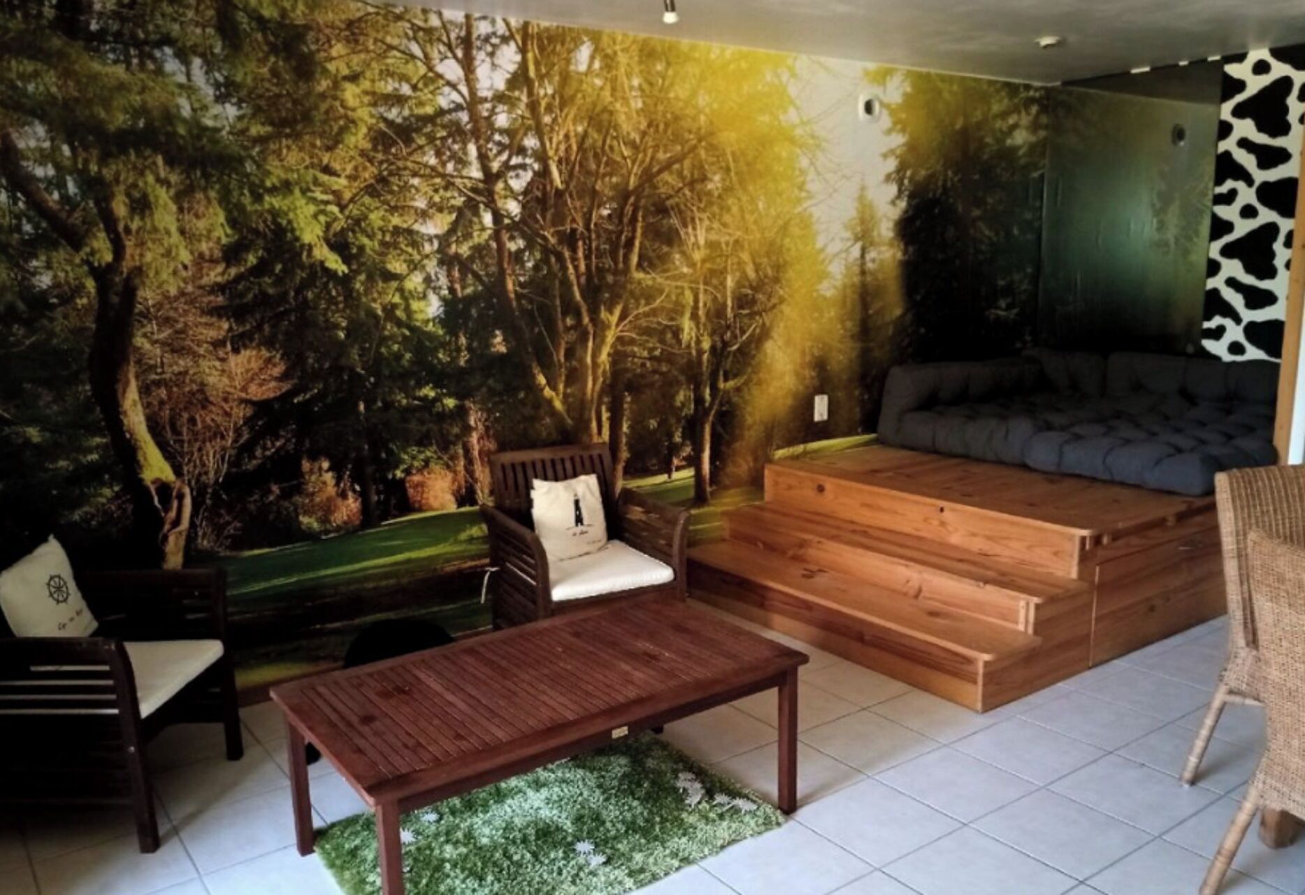 A room with a mural of a forest, a sofa, a wooden bench, a chair, and a small table.