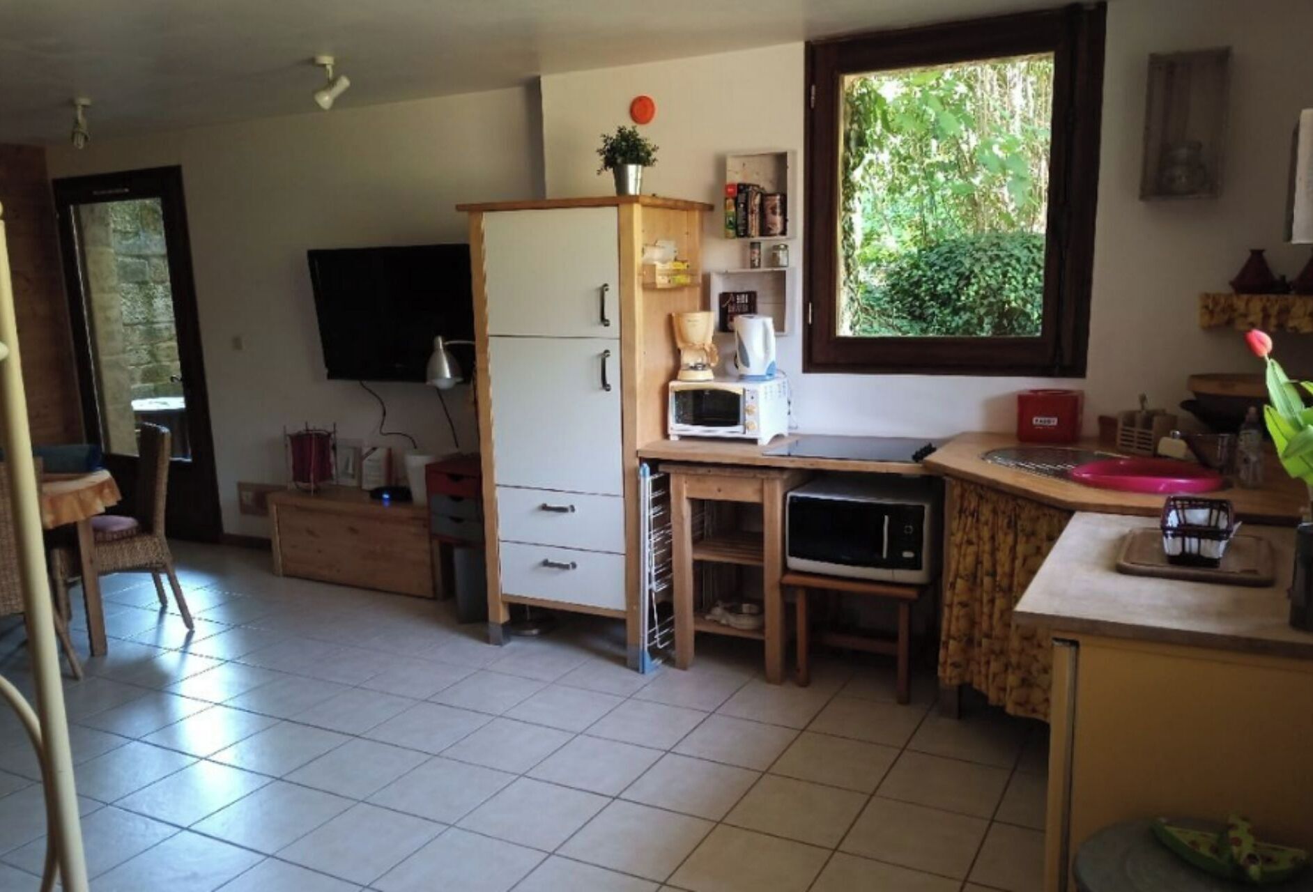 A compact kitchen with a refrigerator, microwave, and coffee maker. There is a window with a view of greenery outside.