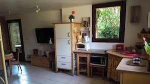 A compact kitchen with a refrigerator, microwave, and coffee maker. There is a window with a view of greenery outside.