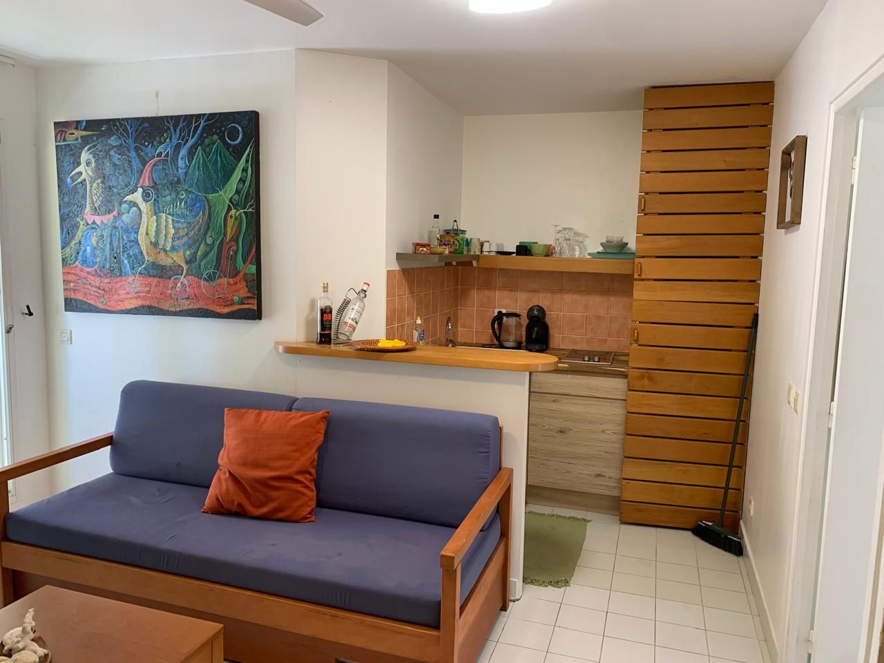 Un salon avec un canapé et un tableau, une cuisine avec une machine à café, et un mur avec des lambris en bois.