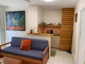 Ett vardagsrum med en soffa och en tavla, ett kök med en kaffebryggare och en vägg med träribbor.