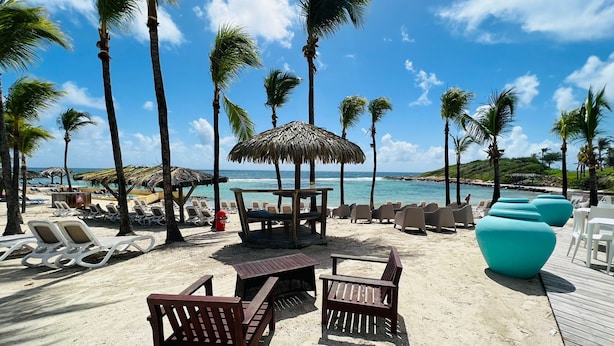 Een strandlounge met ligbedden, een houten tafel en rieten parasols.
