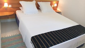 Een opgemaakt bed met witte lakens, twee bedlampen en een gestreepte plaid.