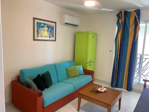 Una sala de estar con sofá, mesa de centro, mueble verde y ventana con cortinas.
