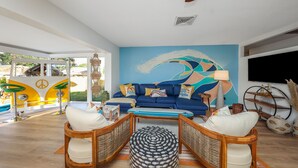 A living room with a blue sofa, wooden chairs, a coffee table, and a mural on the wall. - Tangerine Surfer (Clearwater)