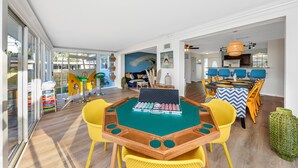 A spacious room with a green felt table for playing cards, yellow chairs, and a large window offering a view of the outdoors. - Tangerine Surfer (Clearwater)