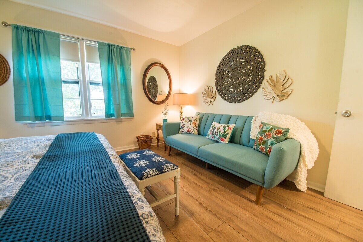 A room with a bed, a blue sofa, a patterned bench, a mirror, and decorative wall art.