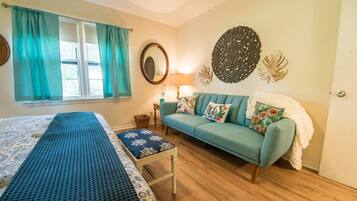 A room with a bed, a blue sofa, a patterned bench, a mirror, and decorative wall art.