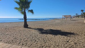 A beach with a palm tree, a wooden deck, and a beach umbrella. - Stylish 2 bed 2 bath property on Duquesa Fairways , 2 terraces,  2 pools (Manilva)