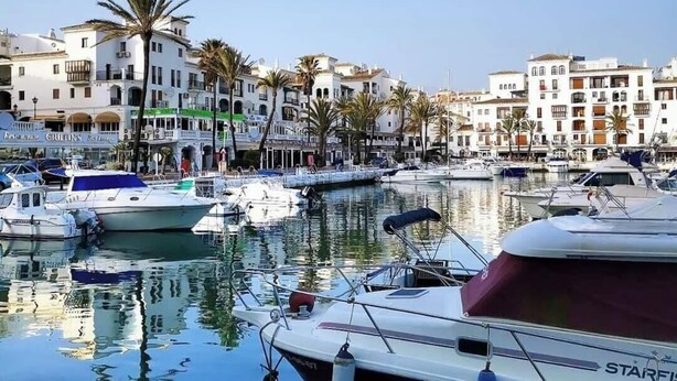 A marina with boats docked, palm trees, and buildings with balconies. - Stylish 2 bed 2 bath property on Duquesa Fairways , 2 terraces,  2 pools (Manilva)