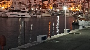 A marina at dusk with boats docked, a waterfront promenade, and buildings with warm lighting in the background. - Stylish 2 bed 2 bath property on Duquesa Fairways , 2 terraces,  2 pools (Manilva)