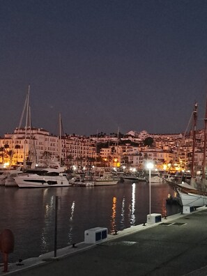 Ein Hafen im Abenddämmerung mit vertäuten Booten, einer Uferpromenade und Gebäuden mit warmem Licht im Hintergrund.