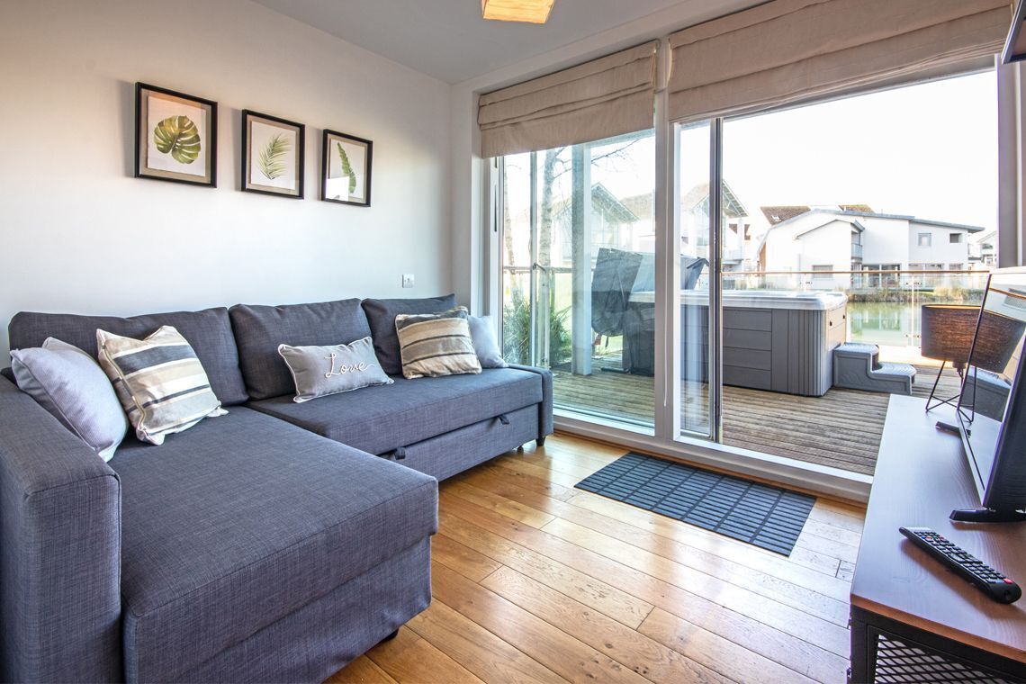 Una sala de estar moderna con un sofá modular gris, piso de madera y un amplio ventanal corredera que da a un área exterior.