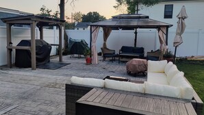 A patio with a covered seating area, a grill, and a covered table. - Homelike, peaceful and centrally- home located in the hamlet of Rocky  Point  NY (Rocky Point)